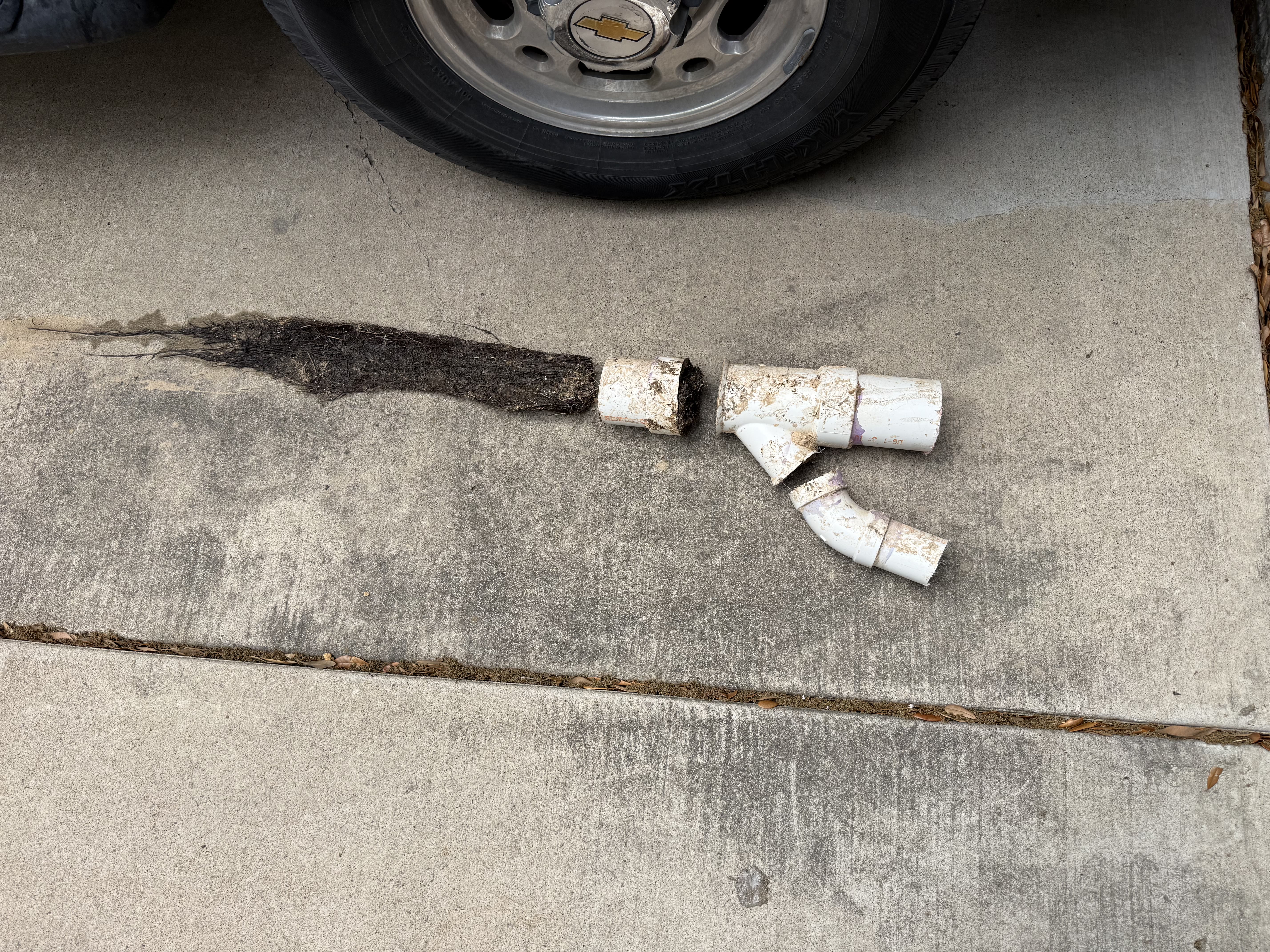 Section of clogged drain pipe with hair and debris pulled out, beside replacement fittings