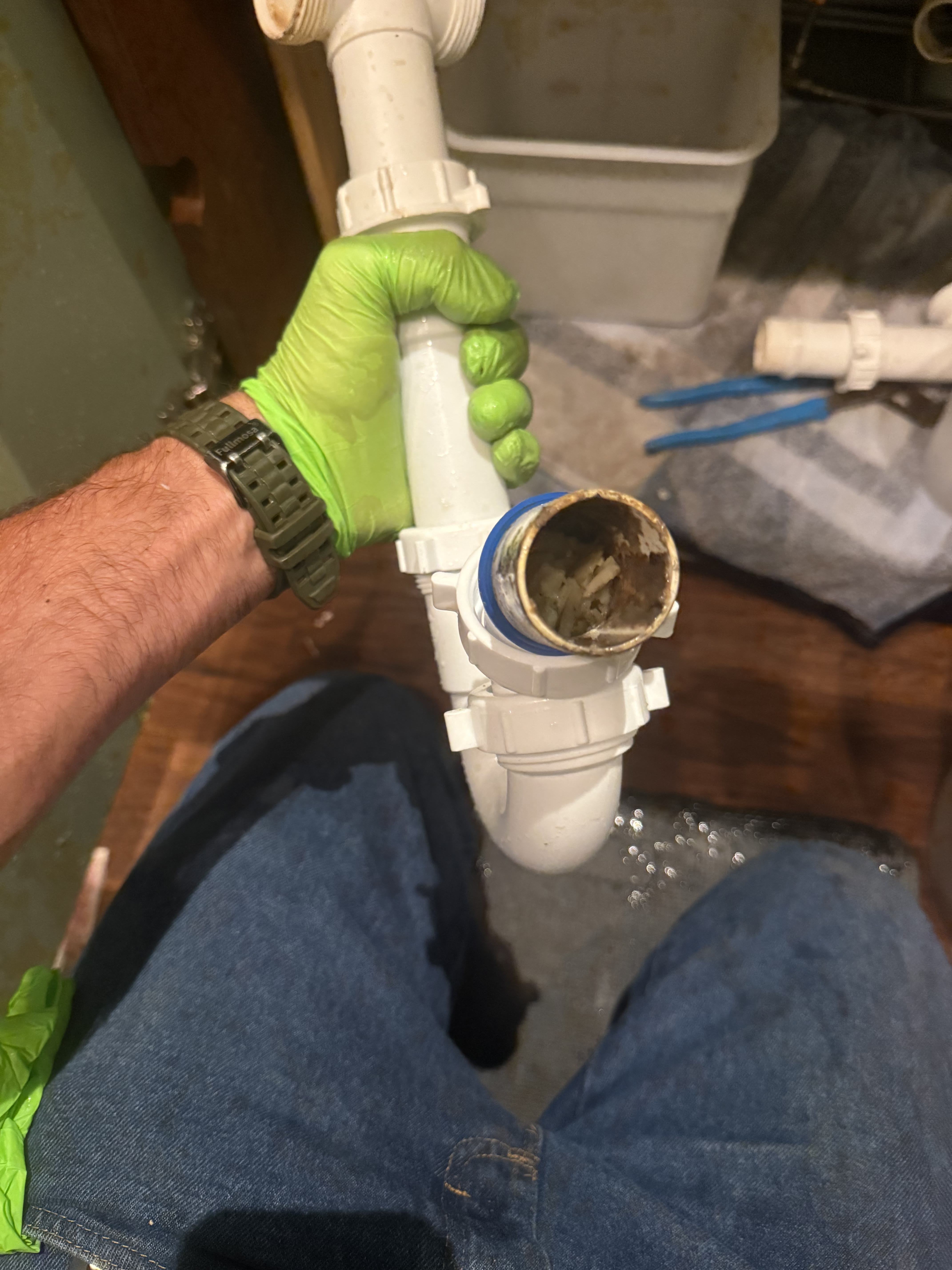 Plumber's gloved hand holding a clogged drain pipe fitting